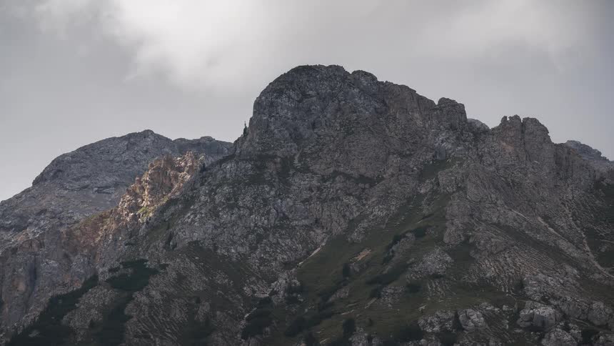 A dramatic timelapse shows shadows and light from fast-moving clouds passing over a rugged mountain peak