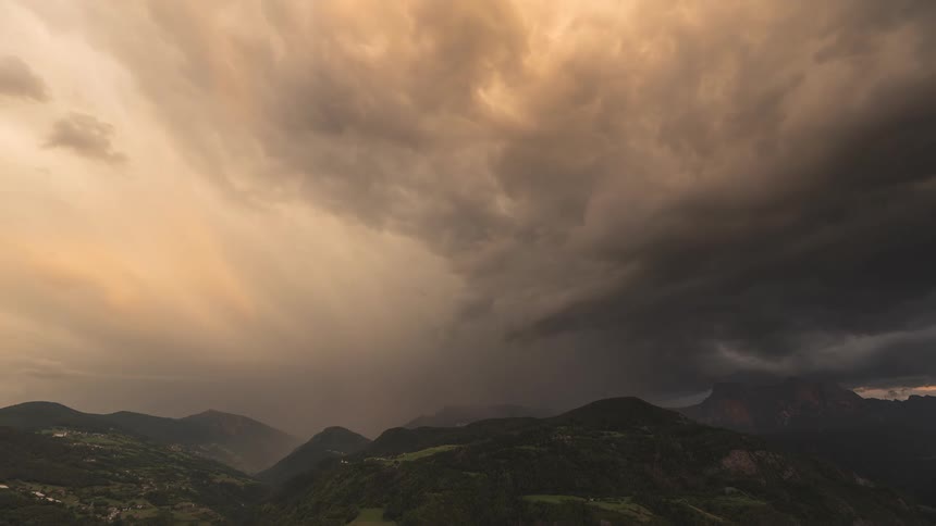 A dramatic timelapse shows golden-hued storm clouds churning and unleashing a torrential downpour over a vast mountain valley