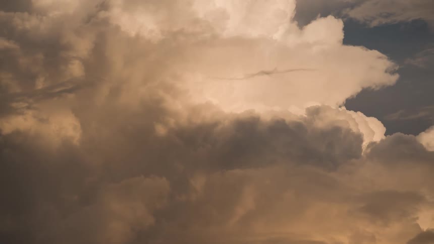 A close view of thick, billowing storm clouds moving slowly with dramatic golden lighting