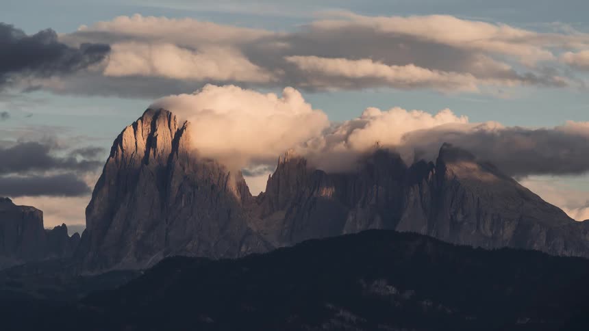 A majestic timelapse of clouds rolling over sunlit mountain peaks during a beautiful golden hour sunset
