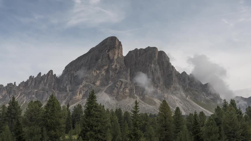 Misty clouds and fog drift and dissipate in a timelapse around a majestic mountain peak above a dense evergreen forest