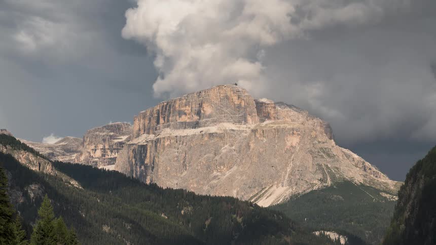 A dramatic timelapse shows dark storm clouds rolling over the sunlit peaks of the Sella Group mountains in the Dolomites