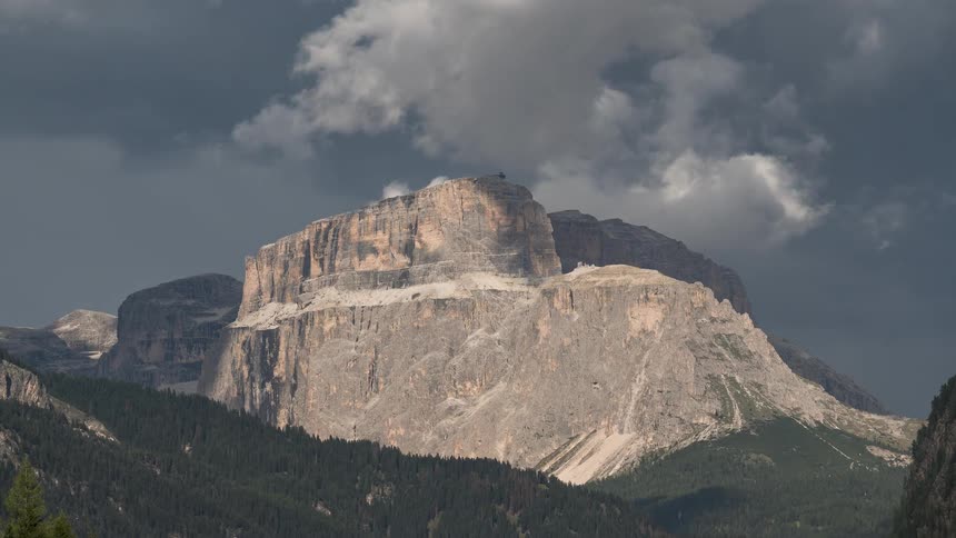 Dramatic storm clouds move across the sky, casting shadows on the majestic Sella Massif in the Italian Dolomites