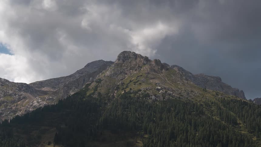 Dramatic storm clouds drift slowly over a majestic, pine-covered mountain peak