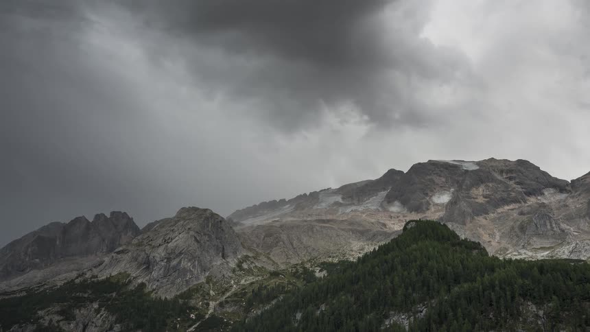 Dramatic timelapse of a powerful storm front with dark, swirling clouds and rain moving over the majestic Marmolada glacier in the Dolomites