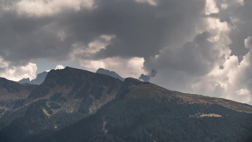 Ominous storm clouds slowly pass over a majestic, tree-covered mountain range