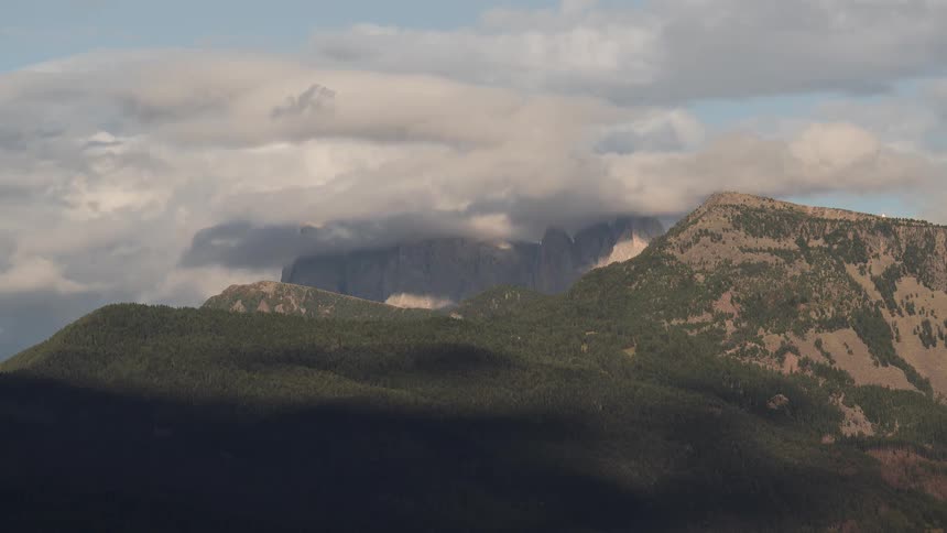 Time-lapse of clouds moving over a majestic mountain range as shadows dance across the forested hills below