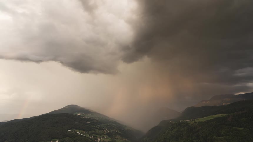 Dramatic time-lapse of a powerful thunderstorm with a faint rainbow passing over a beautiful mountain valley