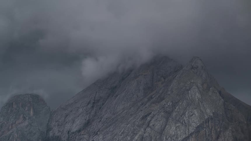 Dramatic timelapse of dark, ominous storm clouds swirling and enveloping a craggy mountain peak