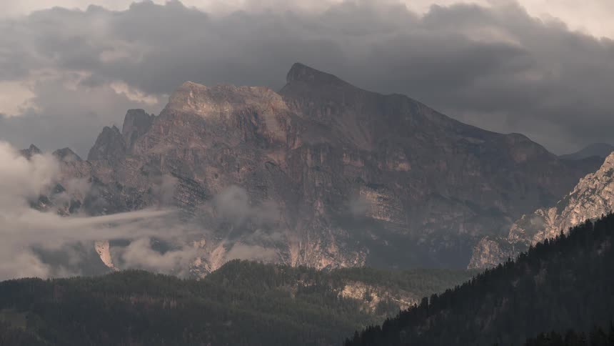 A dramatic timelapse captures clouds and shadows moving across a majestic mountain face