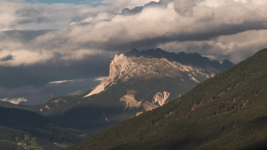 Dramatic timelapse of clouds and shadows moving across the majestic Dolomite mountains as a paraglider soars through the valley