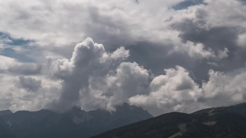 A dramatic time-lapse of large, billowing clouds moving over a majestic mountain range