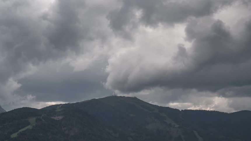 A slow zoom out reveals a forested mountain peak under a sky filled with dramatic and heavy storm clouds