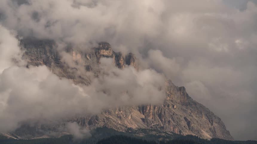 Dramatic clouds drift slowly across the rugged face of a majestic mountain peak