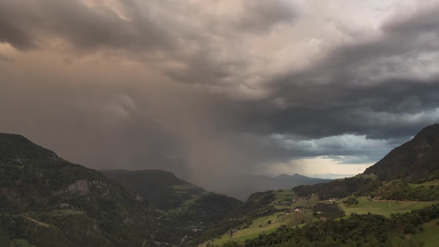 A dramatic timelapse captures a rainstorm sweeping through a verdant mountain valley under dark, rolling clouds