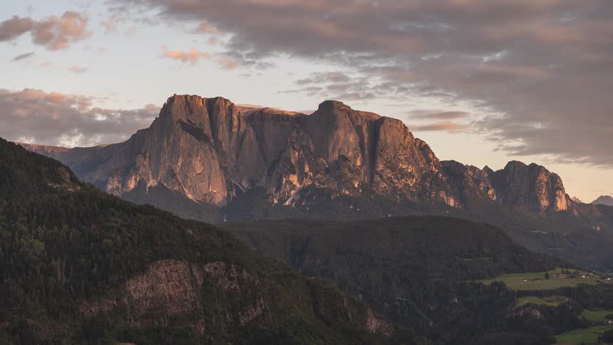 A beautiful sunset timelapse shows the golden light fading across a dramatic mountain range, revealing the shadows of dusk