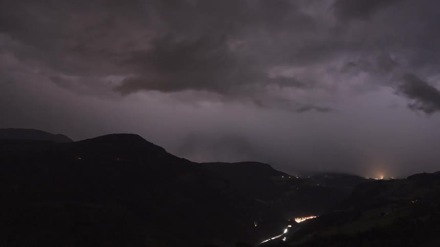 A dramatic time-lapse captures a powerful thunderstorm with constant lightning strikes illuminating a dark mountain valley at night