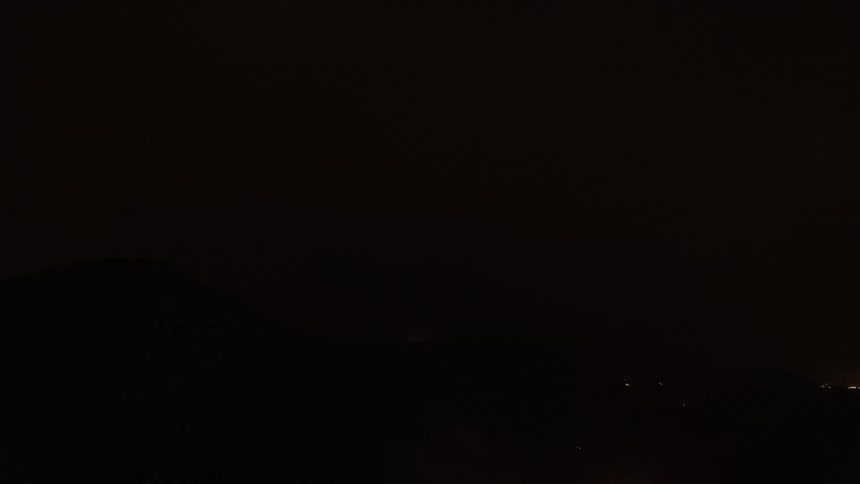 A powerful thunderstorm with frequent lightning strikes illuminates a dramatic mountain range at night