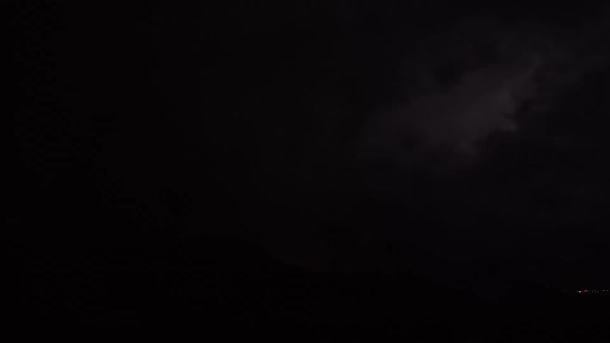 Lightning flashes illuminate a mountain range during a powerful nighttime thunderstorm as viewed through a rain-covered window