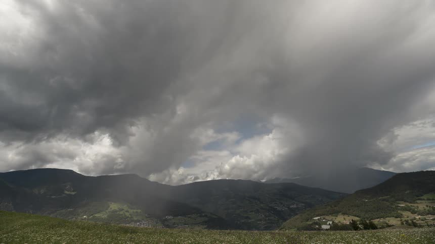 A time-lapse shows dramatic storm clouds gathering and casting shadows over a verdant mountain valley