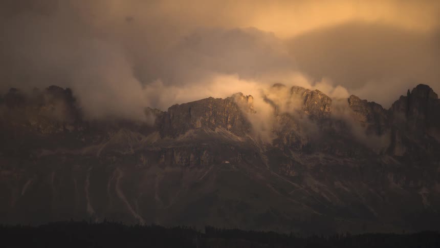 Thick golden clouds illuminated by sunset light drift over a rocky mountain range in a stunning time-lapse