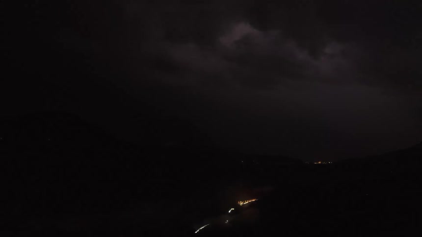 Timelapse of a severe lightning storm raging over a mountain range at night, with fog rolling into the illuminated valley below