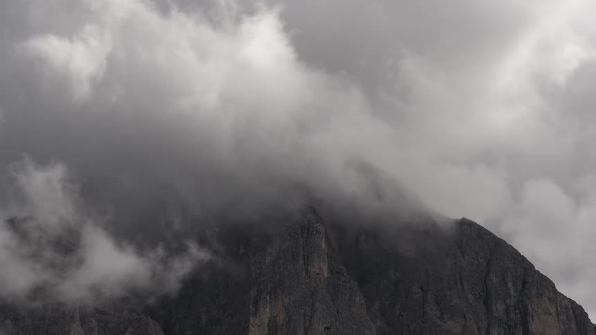 Thick, stormy clouds envelop the peak of a rocky mountain