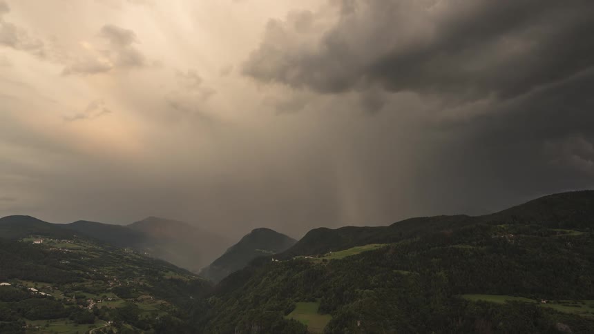 A dramatic timelapse shows a storm with heavy rain moving over a mountain valley, illuminated by golden sunset light