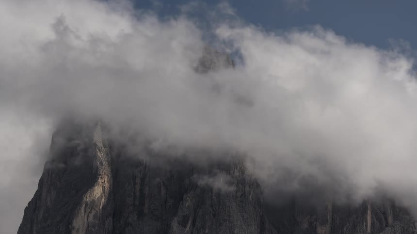 Thick clouds roll over and completely obscure a rugged mountain peak in a stunning timelapse