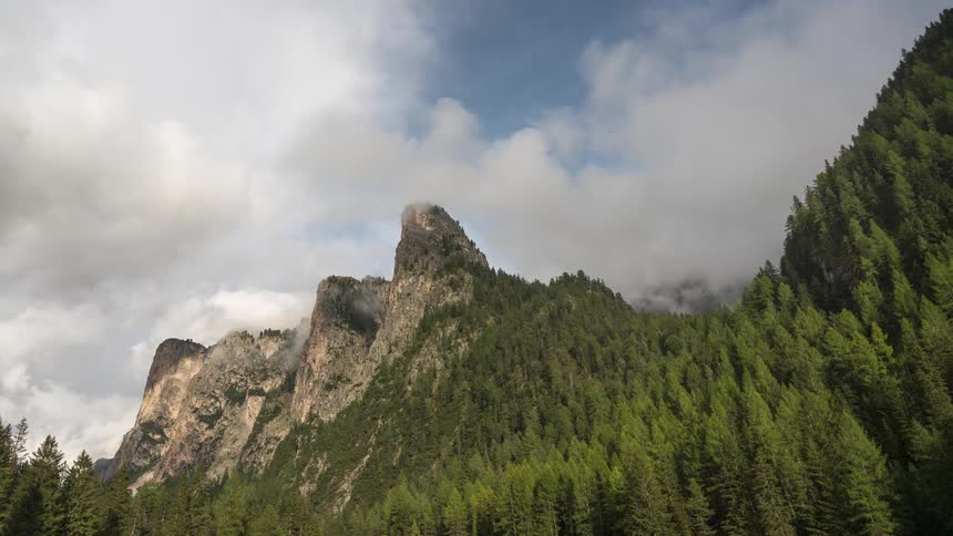 A timelapse of fast-moving clouds rolling over a majestic, forest-covered mountain peak
