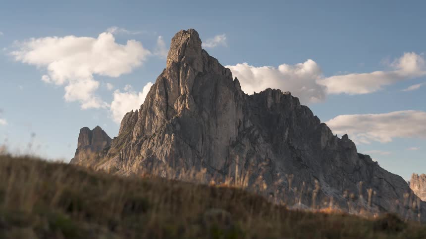 Time-lapse of clouds moving behind the jagged Ra Gusela mountain peak at Giau Pass in the Dolomites, with a grassy meadow in the foreground