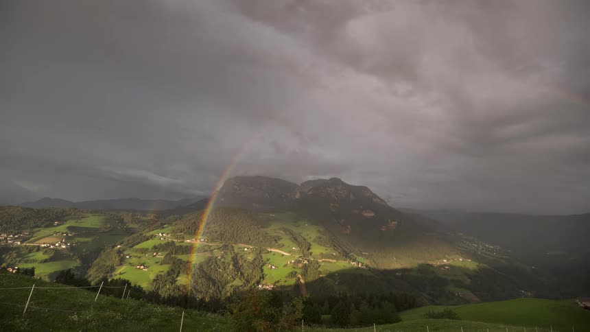 Timelapse footage of a vibrant double rainbow forming over a lush green mountain valley as storm clouds dissipate