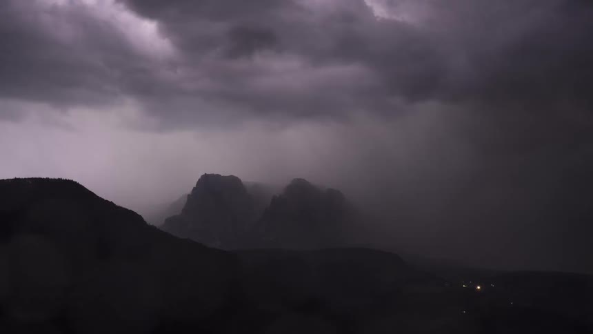 A dramatic lightning storm flashes intensely over a misty mountain range at night