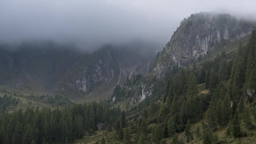 A dramatic time-lapse captures thick clouds and fog sweeping through a mountain valley and evergreen forest