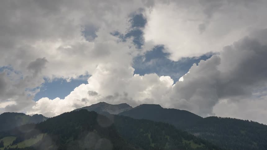 Dramatic white and grey clouds billow over a majestic mountain range as rain begins to fall