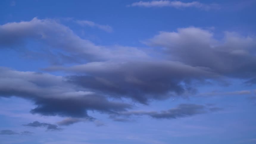 A tranquil view of dark, wispy clouds floating in a blue evening sky as stars begin to appear
