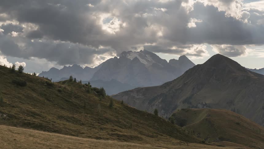 A dramatic time-lapse of sunlight piercing through dark, fast-moving clouds over a majestic mountain range