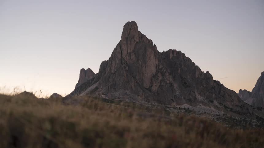 A stunning timelapse captures the golden sunset light fading into a purple twilight sky over a majestic mountain peak