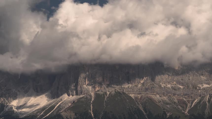 A dramatic timelapse captures dark, swirling clouds moving over the rugged peaks of a majestic mountain range