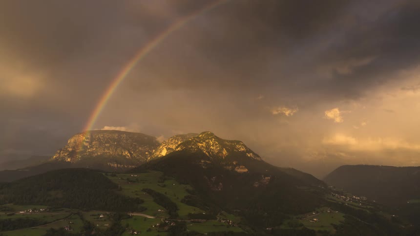 A stunning timelapse of a rainbow arcing over a mountain range while storm clouds pass during a golden sunset