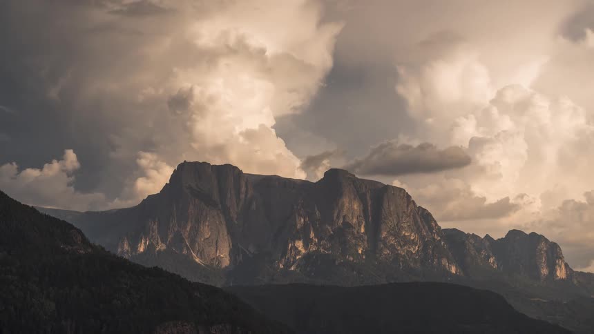 Dramatic golden hour light illuminates a rugged mountain range as storm clouds billow and move across the sky in a time-lapse