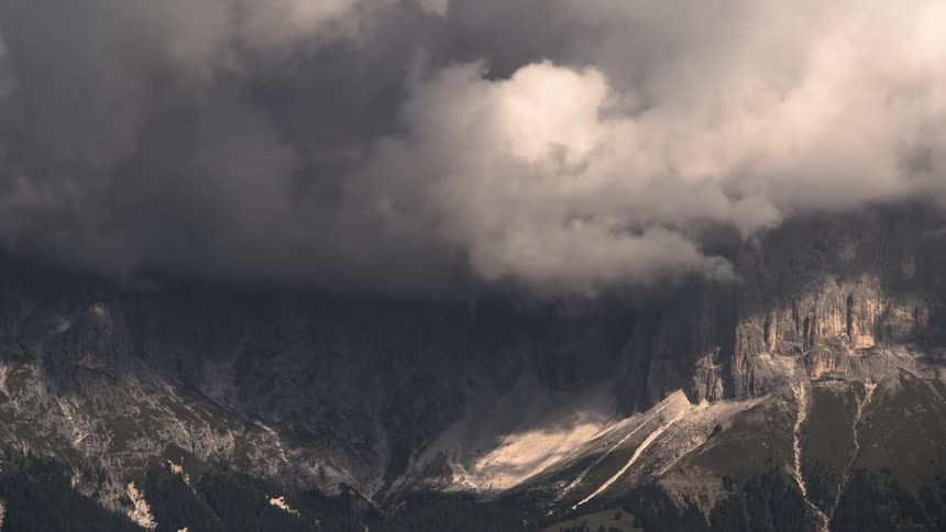 A dramatic, stormy sky with dark clouds rolling over a rugged mountain range as sunlight breaks through
