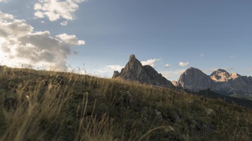 A serene timelapse of clouds moving over majestic mountain peaks as the rising sun illuminates a grassy alpine meadow