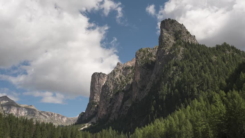 Majestic, tree-covered mountains stand tall as clouds drift slowly across a brilliant blue sky