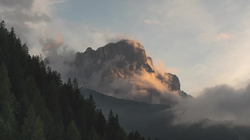 A time-lapse shows clouds illuminated by the setting sun as they envelop a rugged mountain