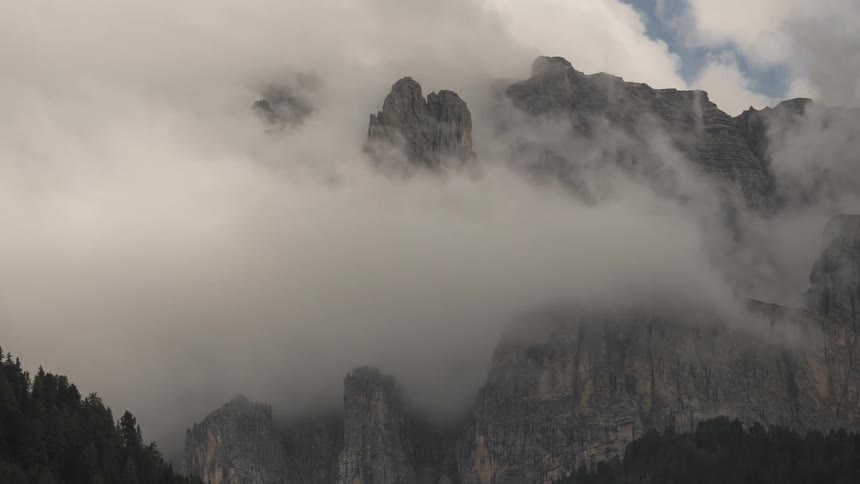A dramatic timelapse captures thick, swirling clouds as they completely engulf a rugged mountain peak