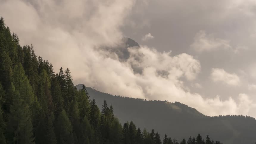 A stunning timelapse shows clouds swirling around a majestic mountain peak behind a lush evergreen forest