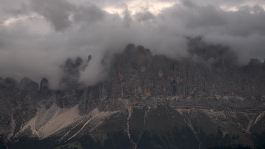 Majestic mountain peaks are slowly revealed and concealed by thick, rolling storm clouds