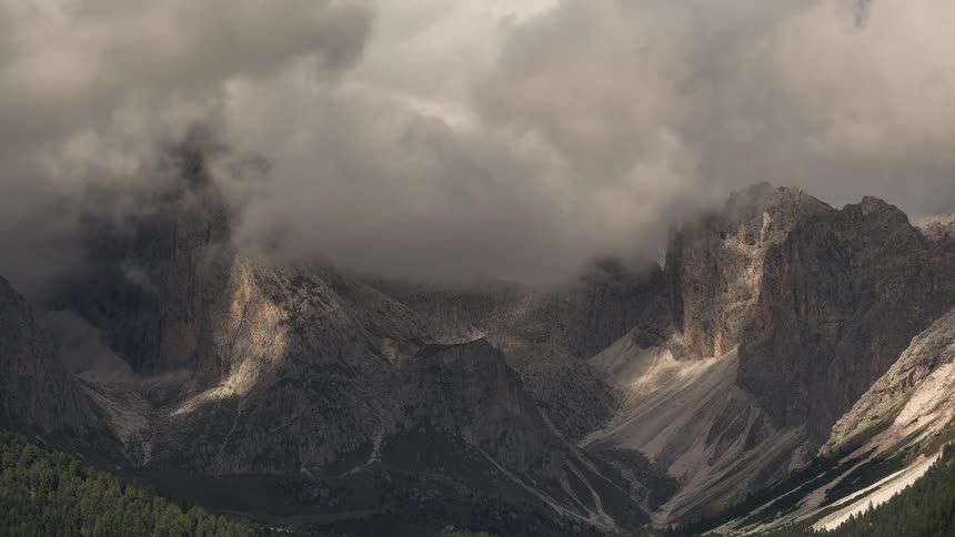 Dramatic time-lapse of moody clouds rolling over majestic mountain peaks, creating shifting patterns of light and shadow