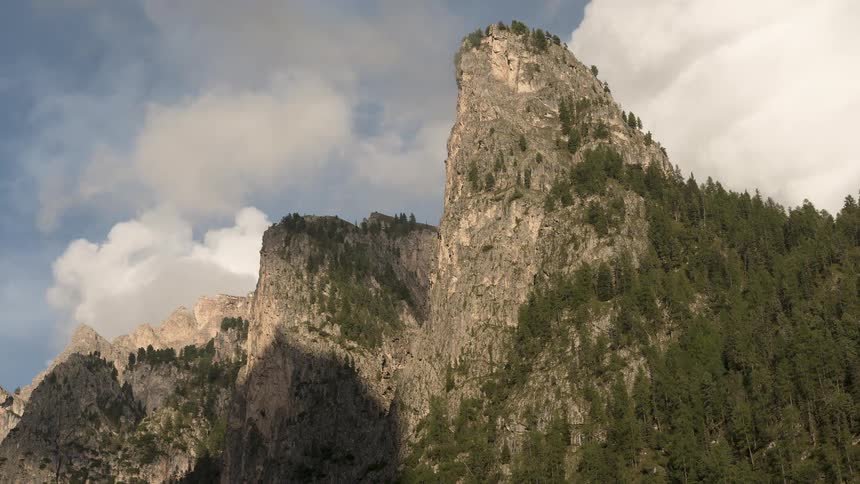 A beautiful timelapse captures clouds moving across a majestic rocky mountain peak covered in lush green pine trees